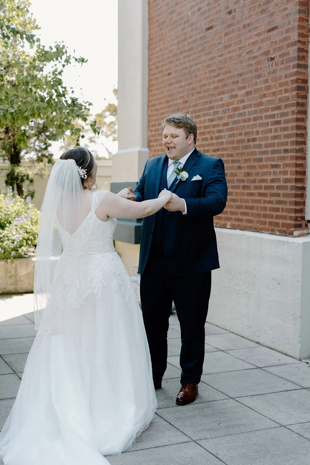 Bride and groom holding hands with groom smiling at bride at first look