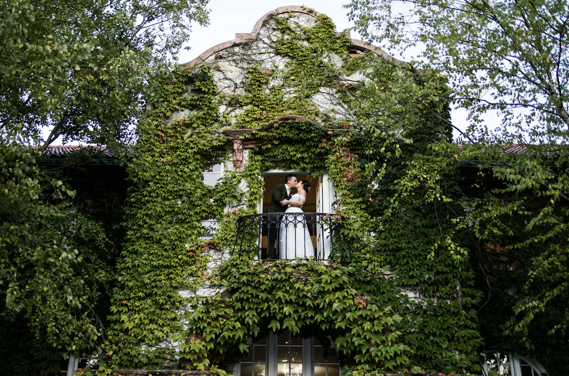 Bride and groom kissing on balcony with ivy walls all around them