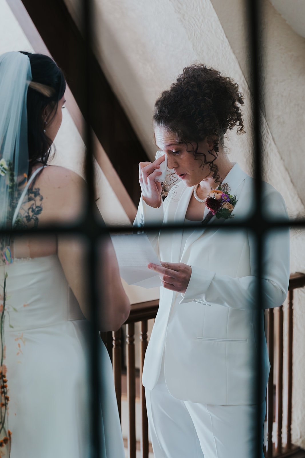 Bride in suit wiping tear away while reading vows to bride in dress