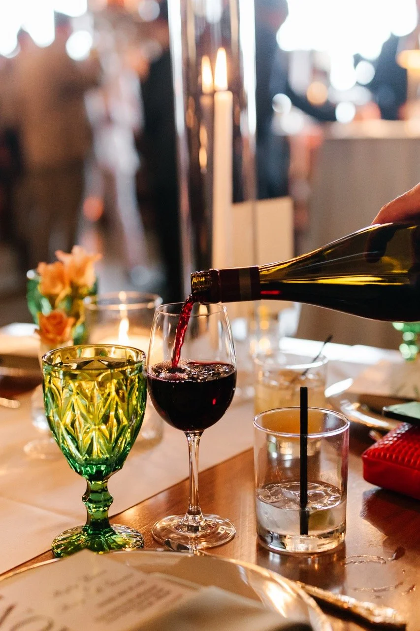 Red wine poured into glass with other glasses on the table for cocktails and water for wedding dinner reception