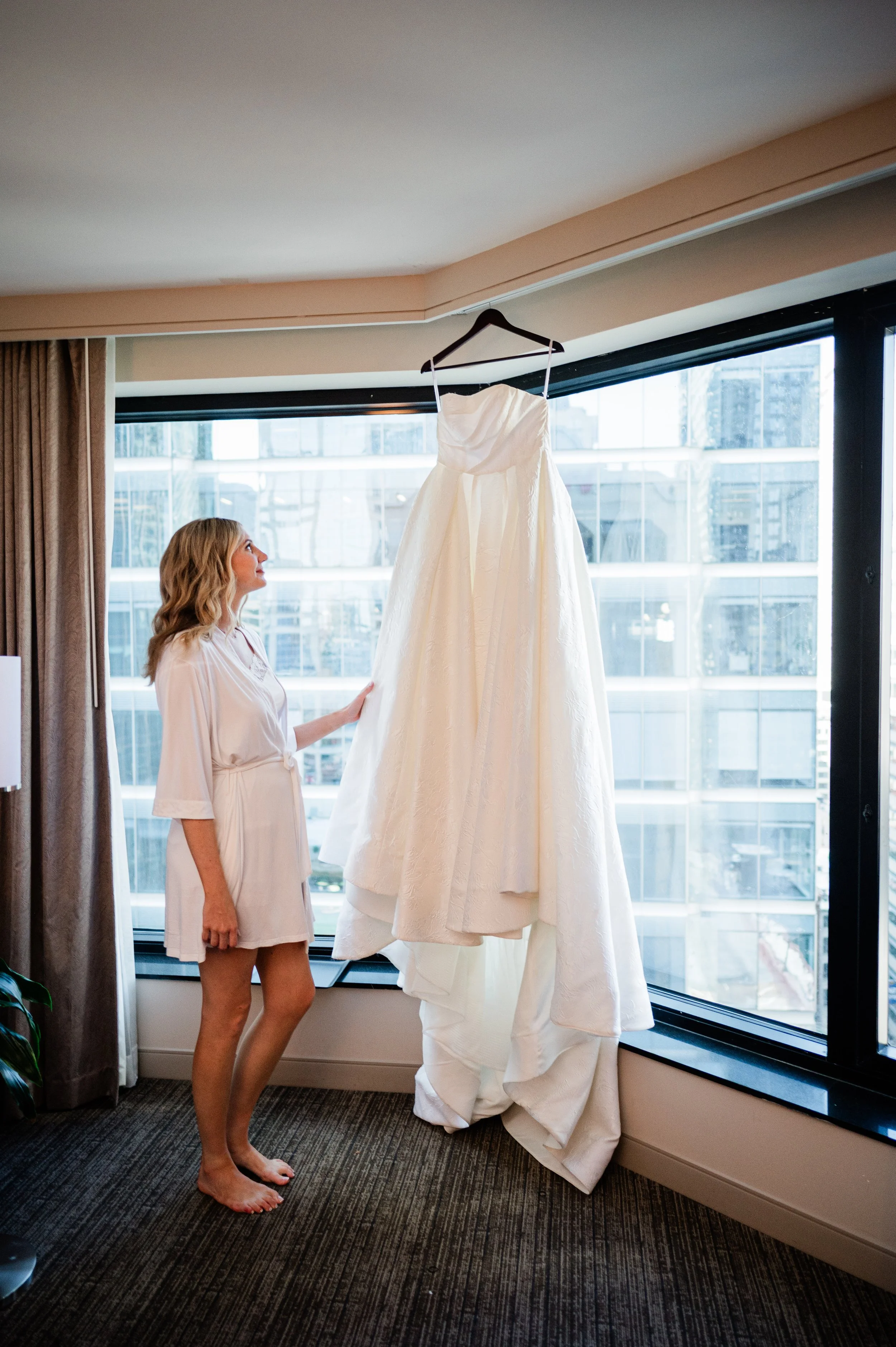 Bride looking at hanging wedding dress in hotel getting ready location