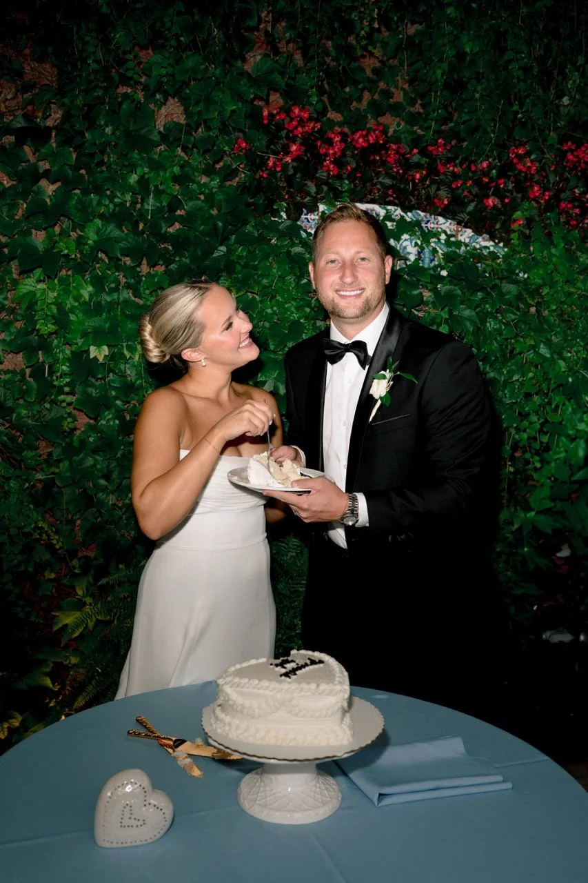 Bride smiling at groom while both are holding and sharing a plate with a piece of cake after cutting it