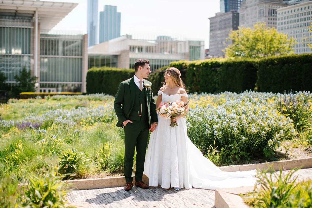 Bride and groom outdoors looking at each other and smiling with green foliage all surrounding their path