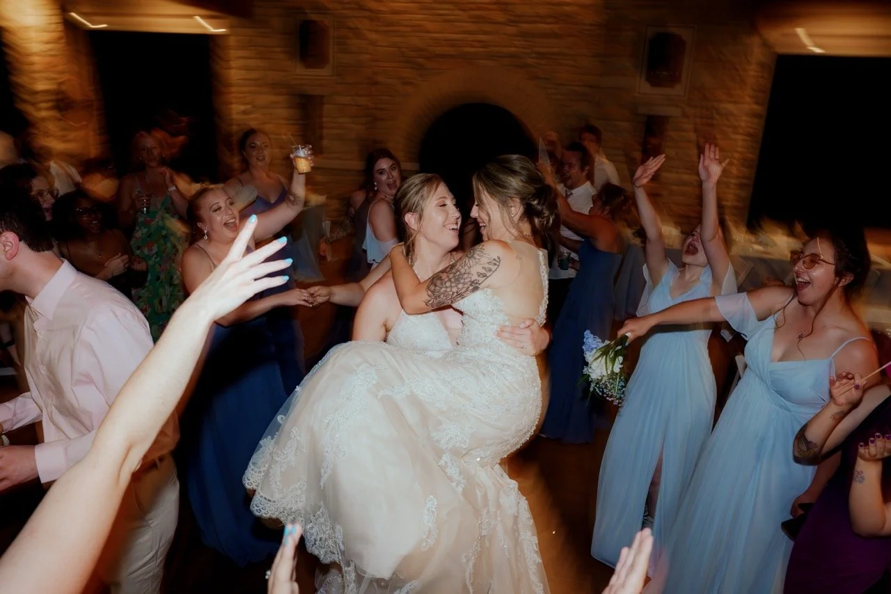Bride in tulle holding bride in lace in her arms on wedding reception dance floor