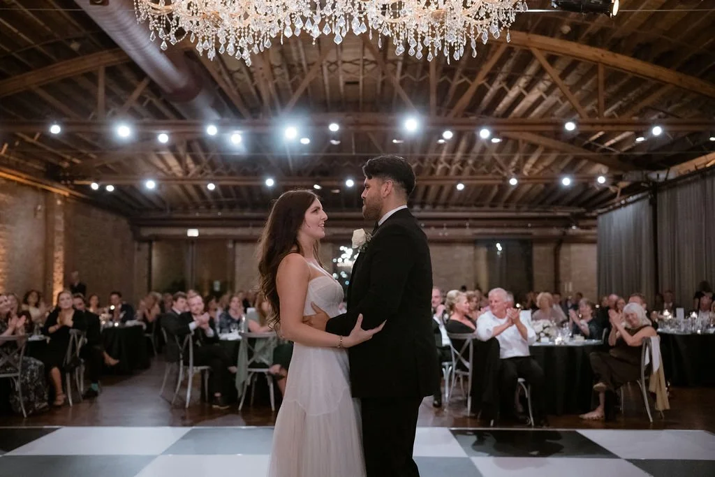 bride and groom first dance with wedding guests in the background