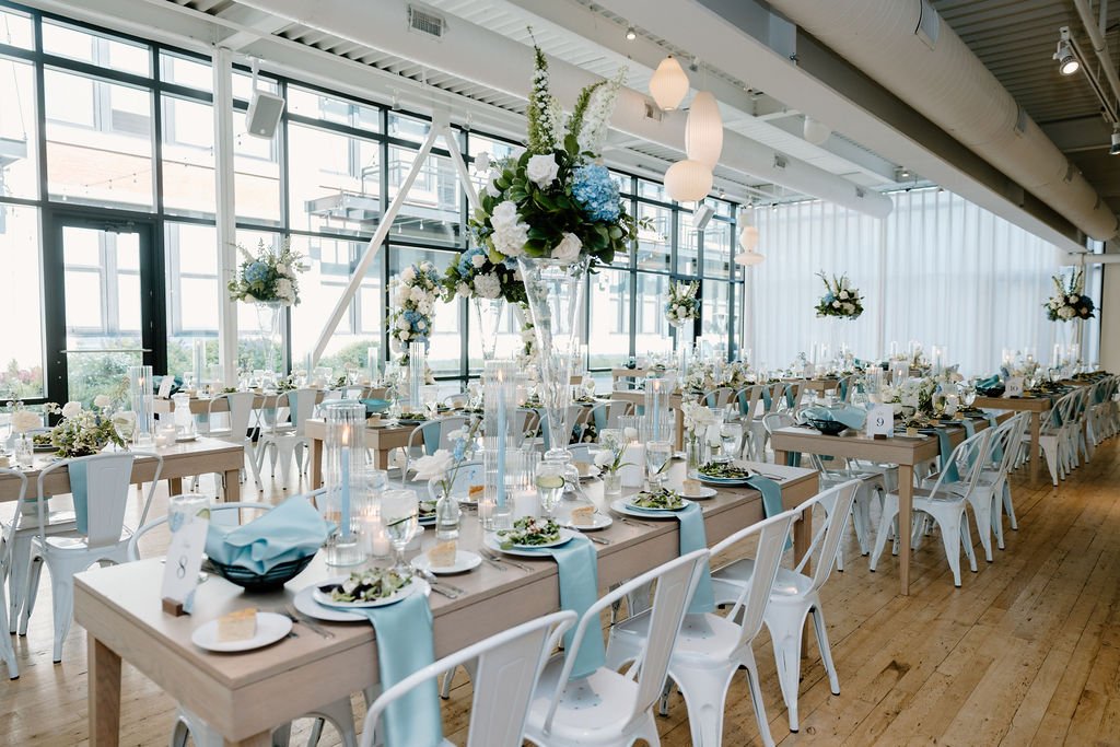 Full room shot of tables, chairs, candles, and centerpieces all white and light blue