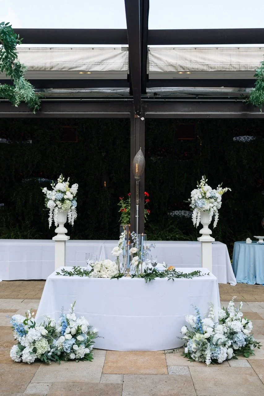 Sweetheart table with floral pillars and flowers on ground in front of white table