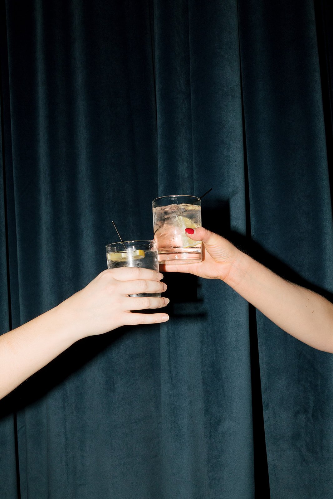 Two people cheersing cocktails with blue velvet curtain as background during cocktail hour