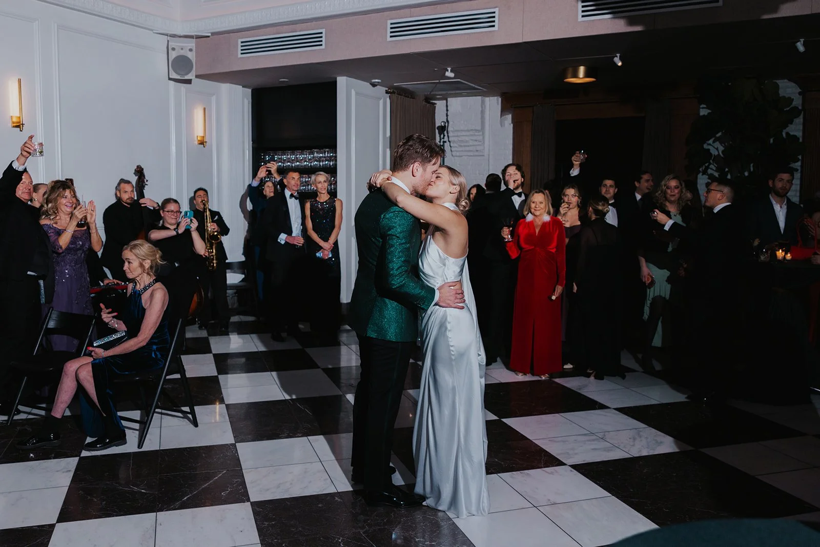 couple kissing on black and white checkered dance floor with guests circling around them