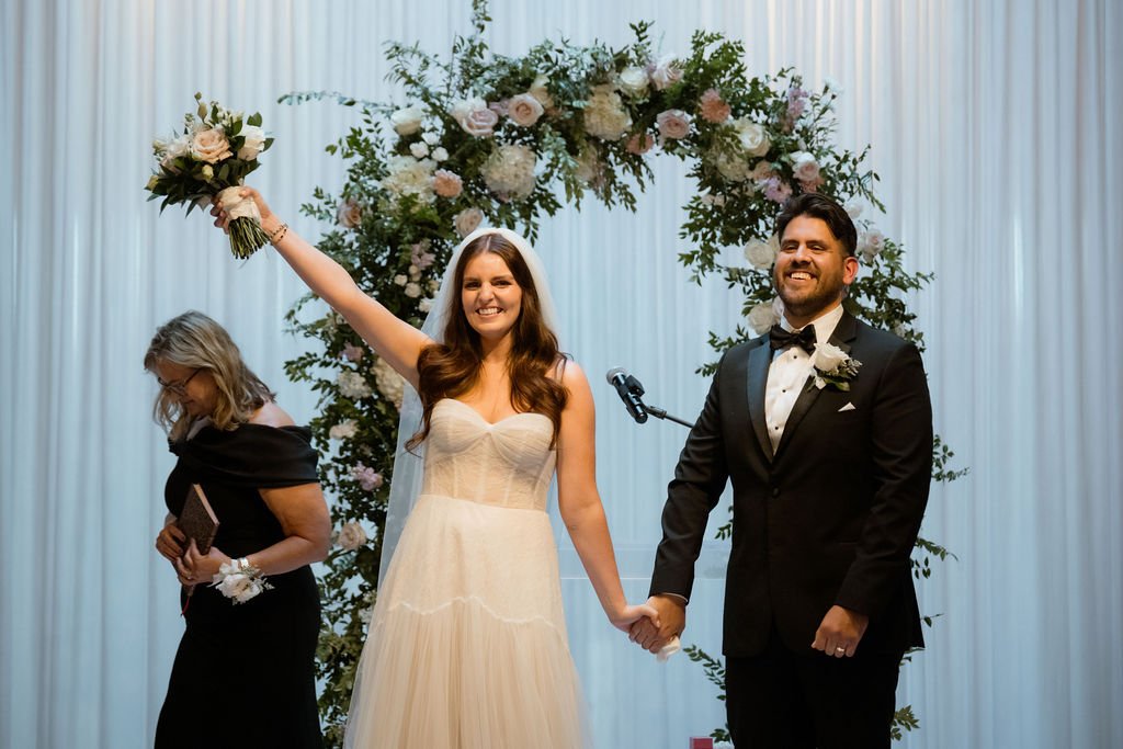 Bride raising bouquet and couple smiling toward crowd after wedding ceremony just married