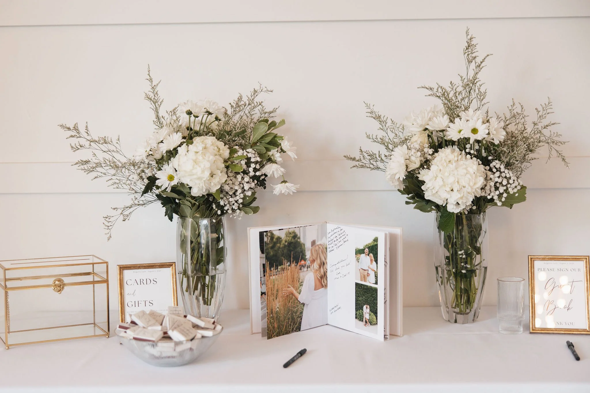 Welcome table with card box, flowers from ceremony, and editorial signed guest book with engagement photos