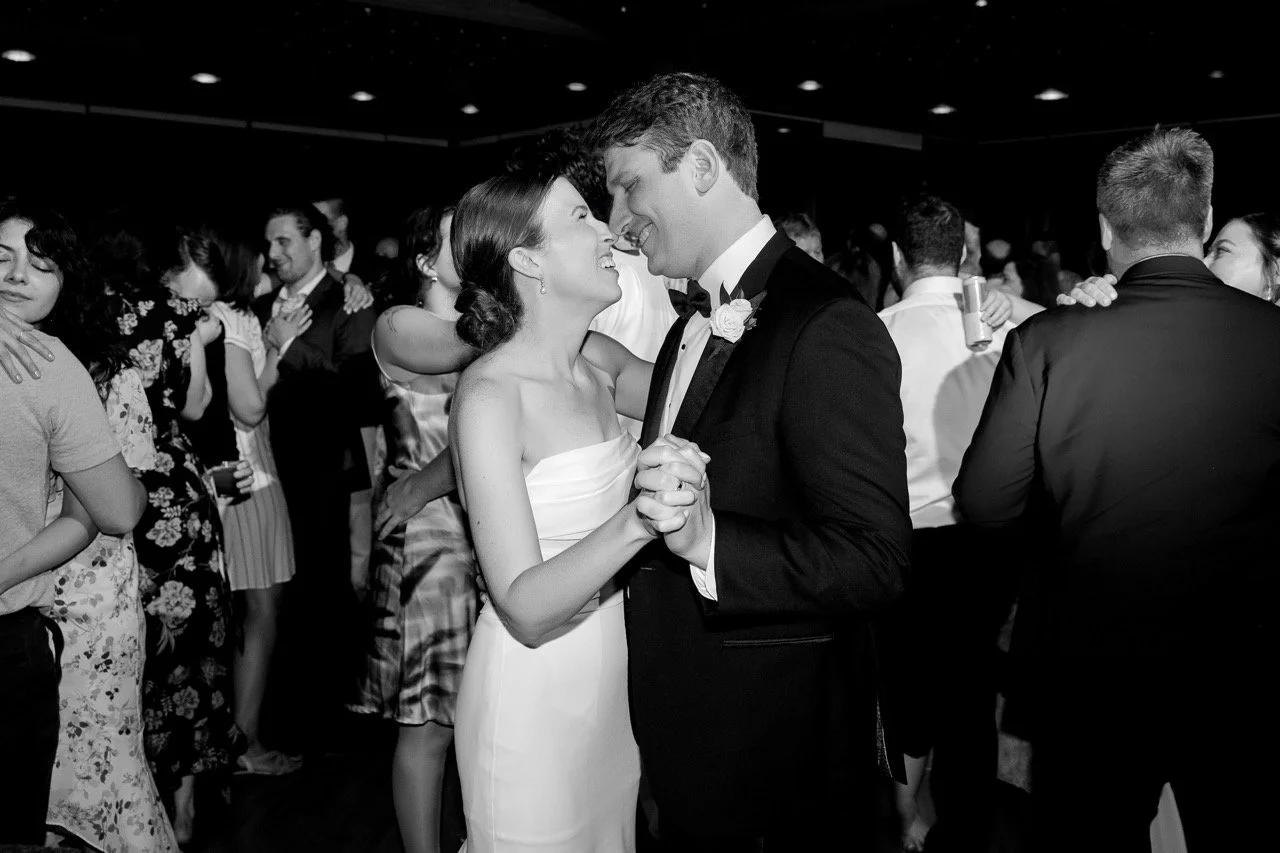 Black and white photo of couple dancing with wedding guests on dance floor