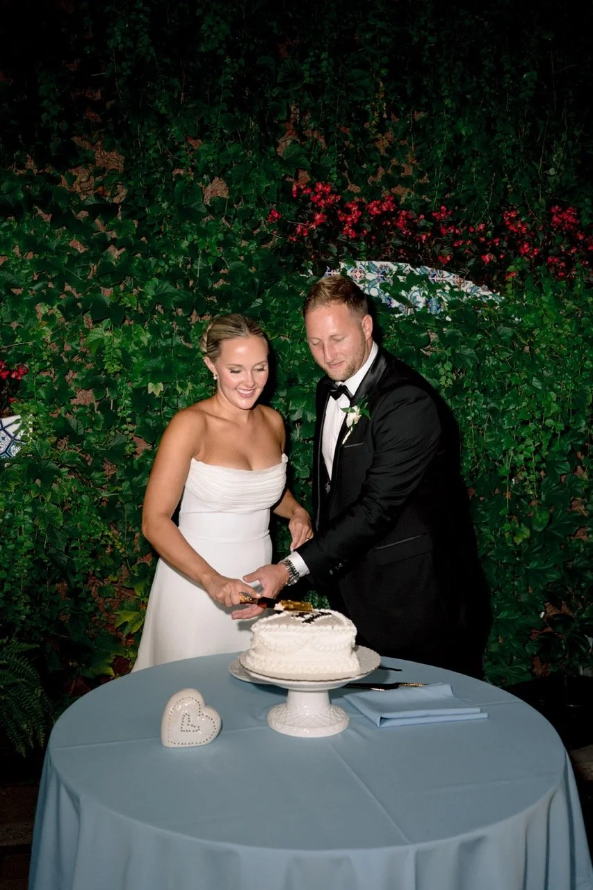 Bride and groom standing behind table with small cake for cutting at wedding reception