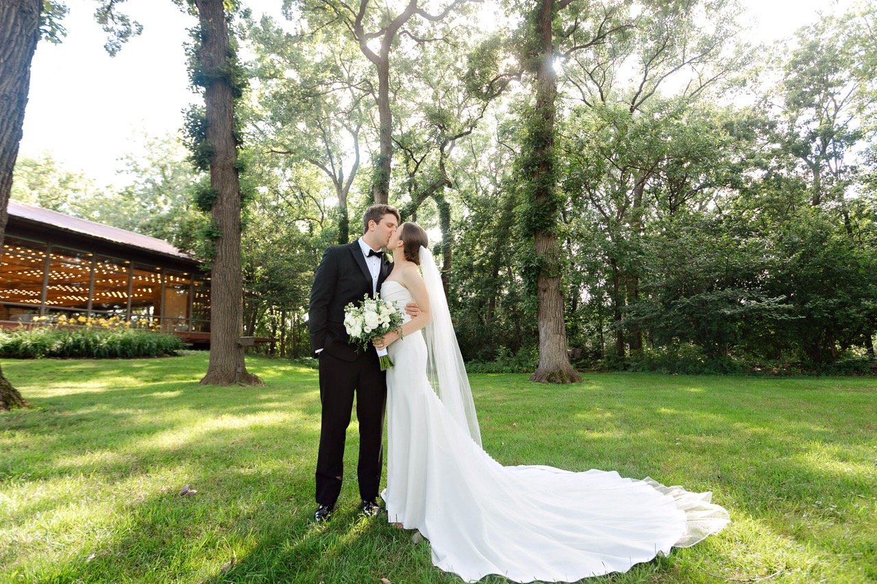 Bride and groom kissing in outdoor grassy area of Hyatt Lodge Grand Oaks Pavilion in background