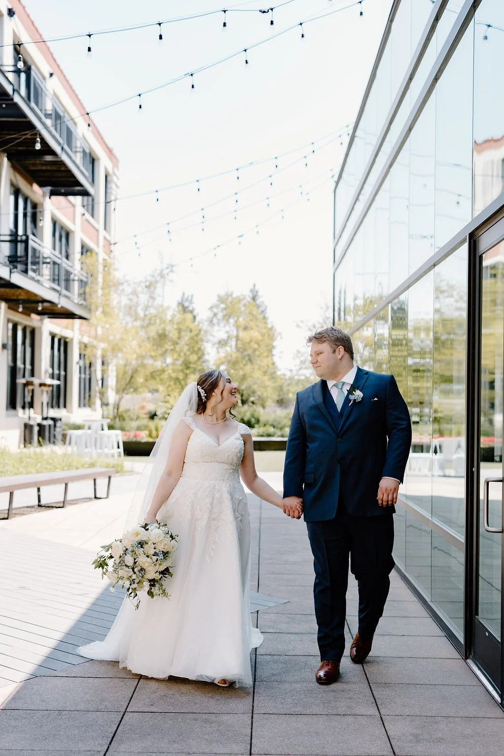 Bride and groom looking at each other holding hands and walking with sunny background