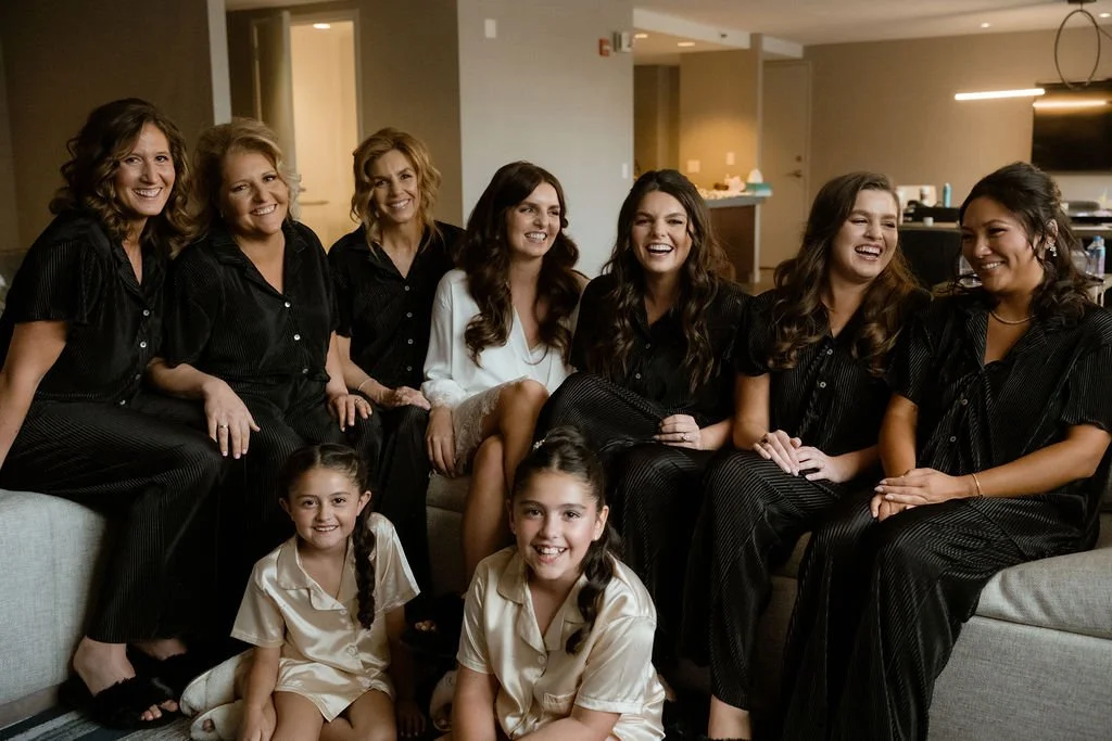 Bride sitting with bridesmaids in black and white getting ready pajamas laughing together for Chicago wedding
