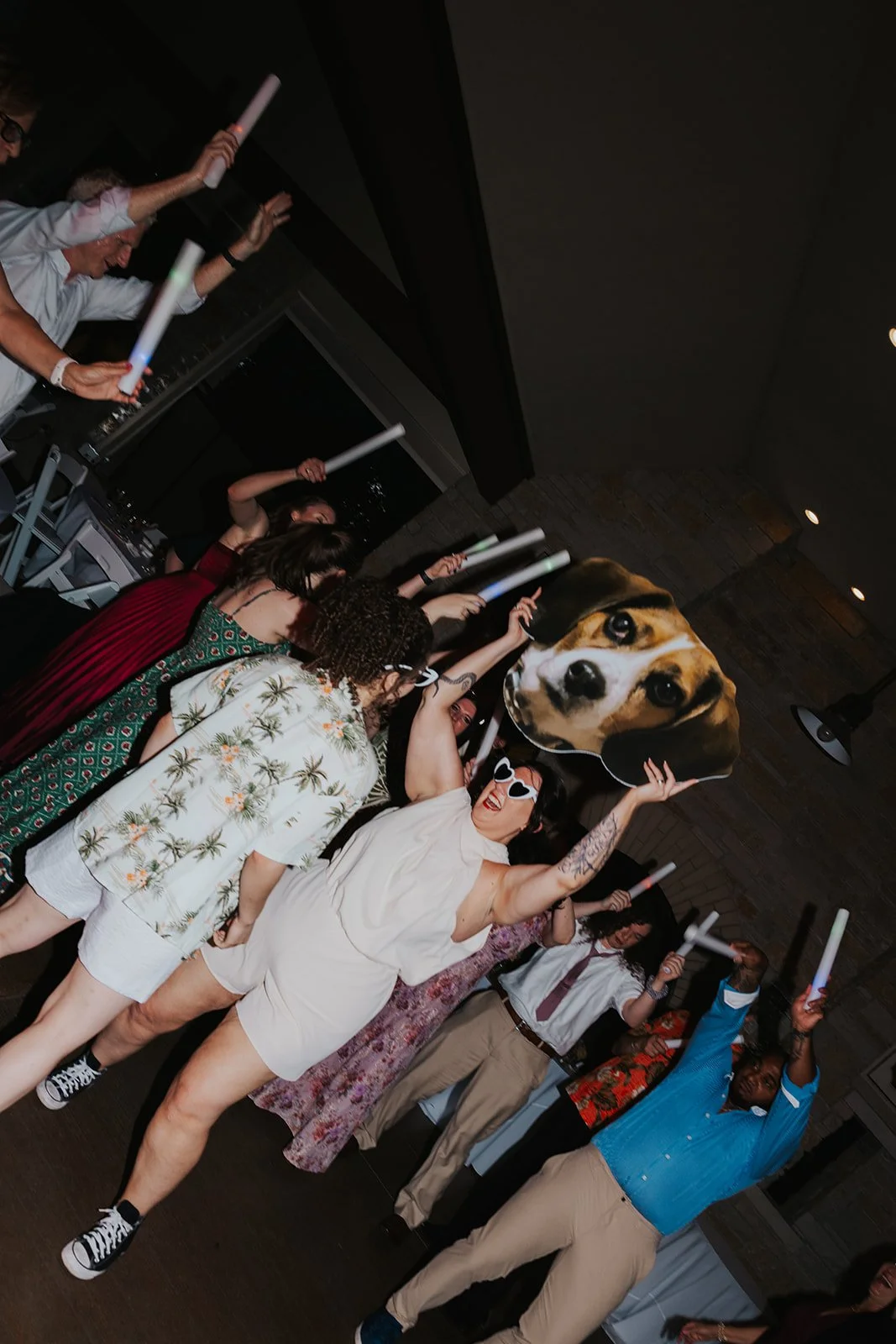 Two brides dancing together and one holding a huge fat head of their beagle with guests dancing on dance floor