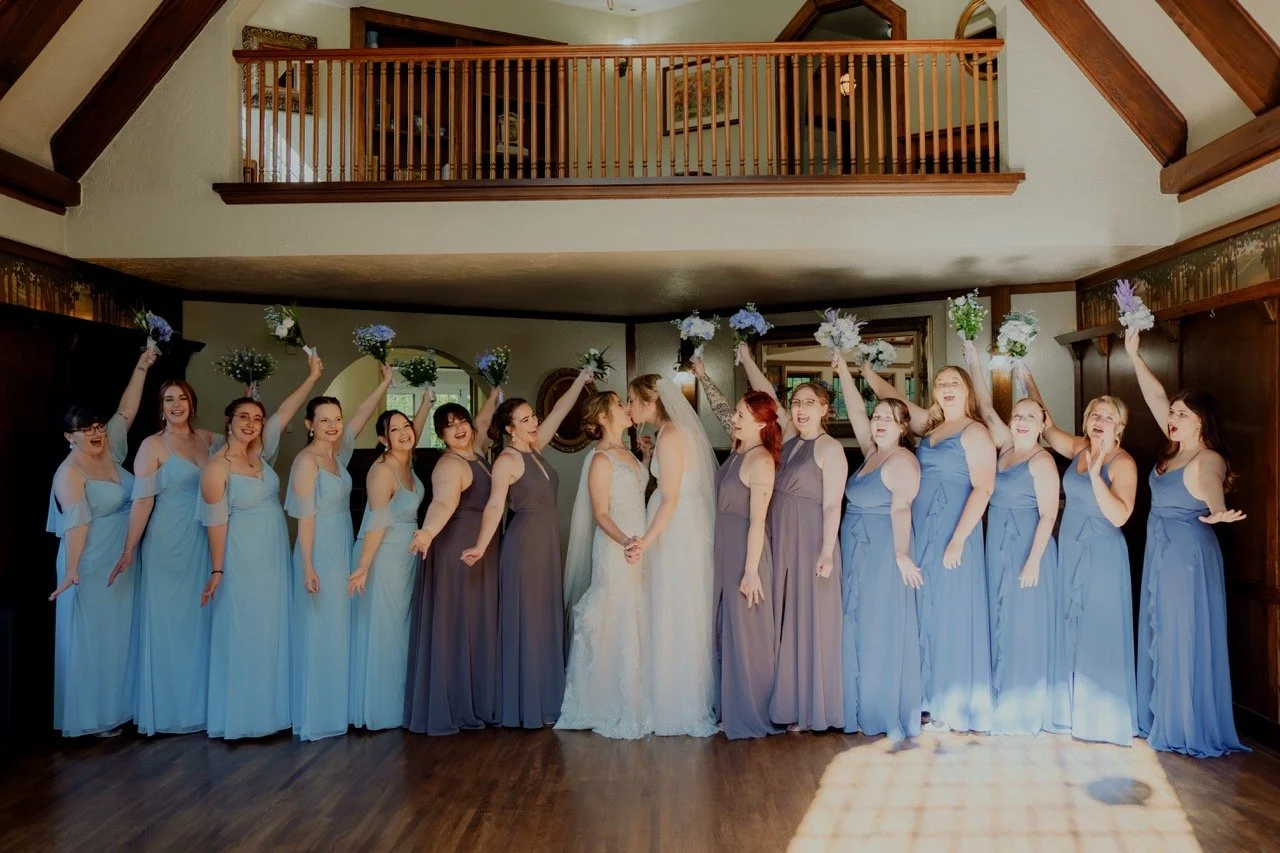 Inside the Redfield Estate home with two brides and bridesmaids cheering while couple kisses