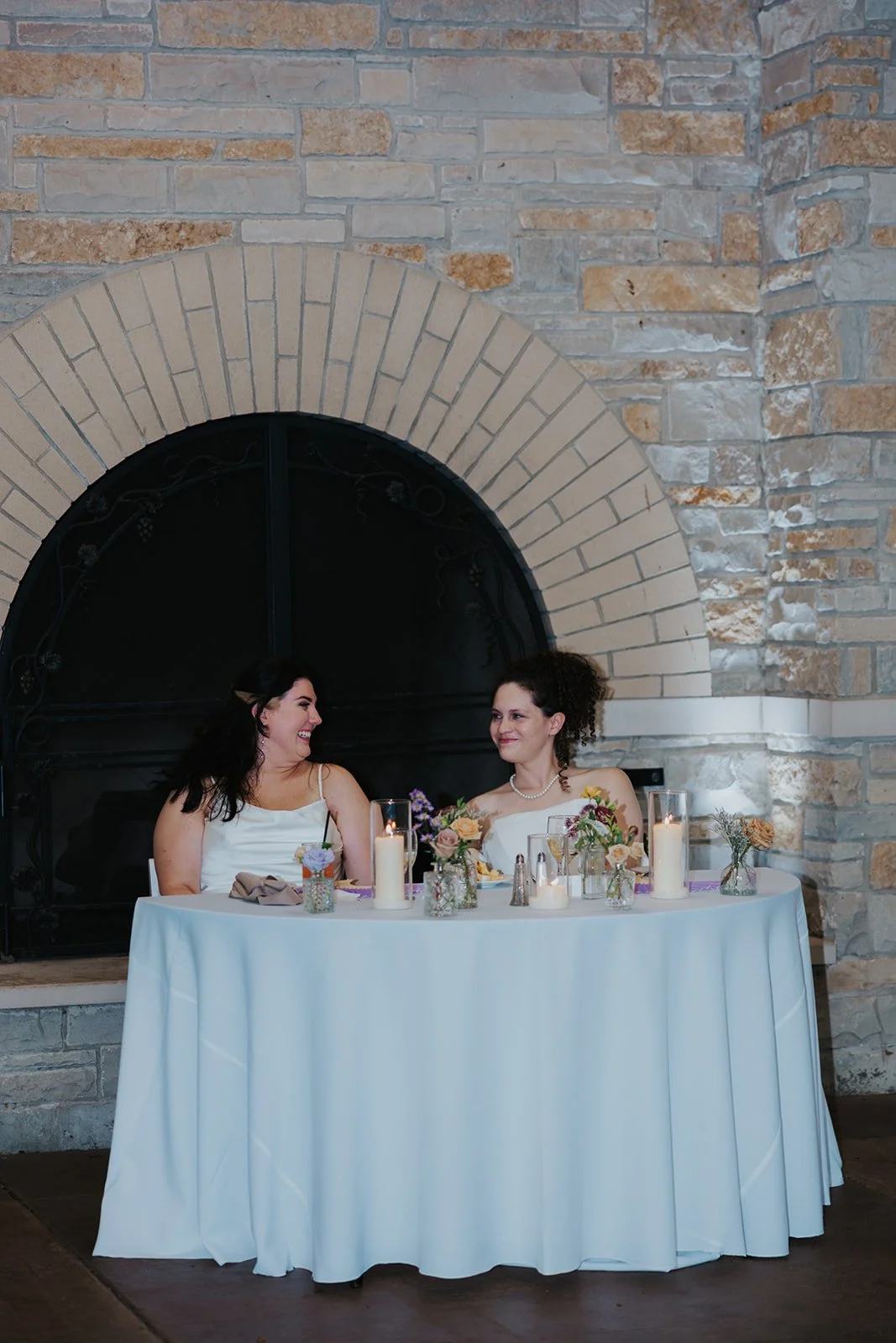 Two brides sitting at sweetheart table looking at each other and smiling