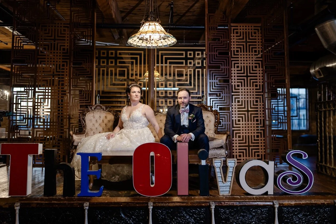 Bride and groom sitting on couch on stage with eclectic letters spelling out their last name in front