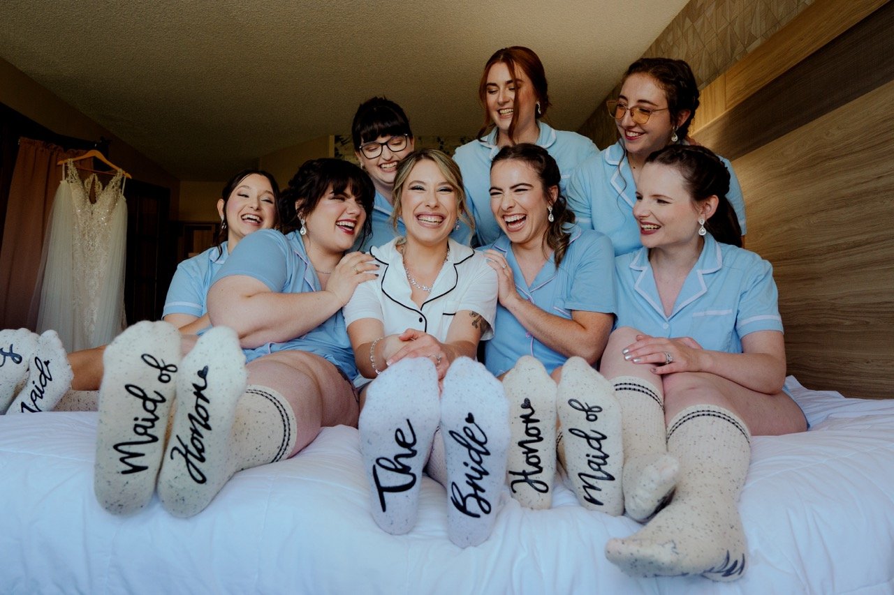 Bride and bridesmaids sitting on bed with light blue and white pajamas and socks that say "bride" and "bridesmaid"