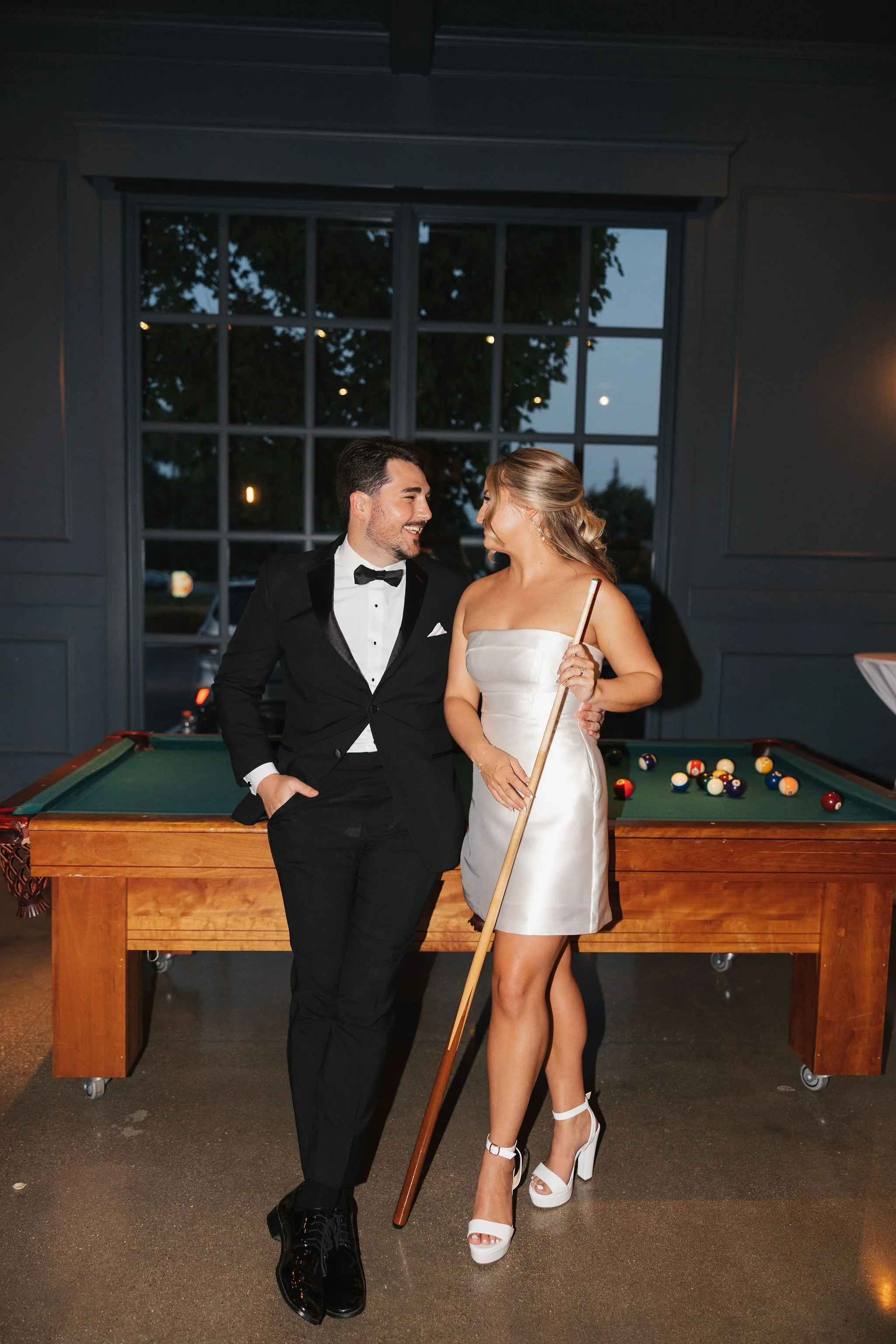 Bride in new reception dress and looking at each other leaning against pool table