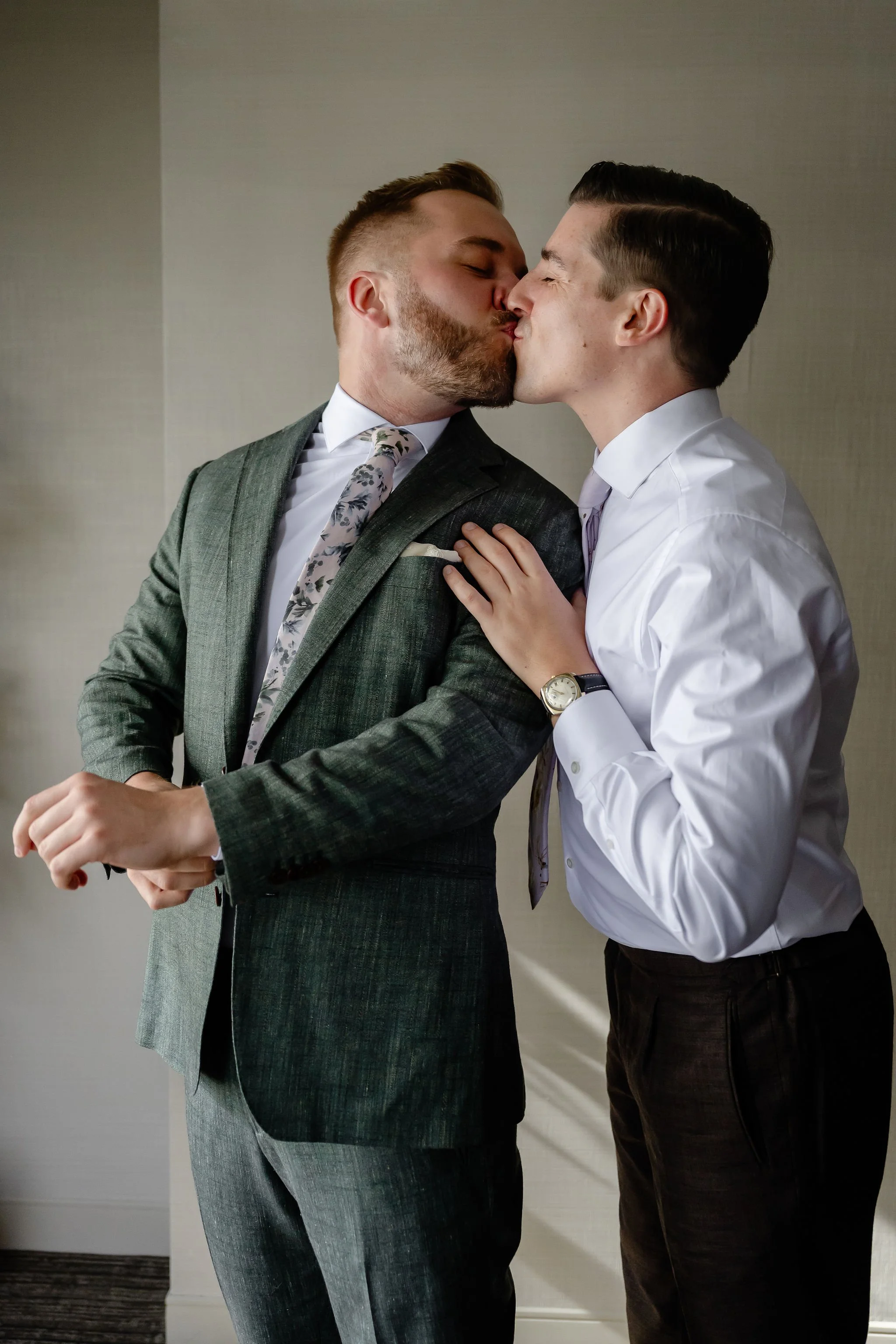 Two grooms getting ready together and kissing while getting ready for wedding