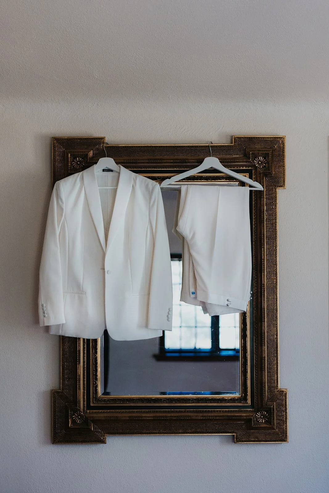 white suit jacket and pants hanging from hangers on mirror