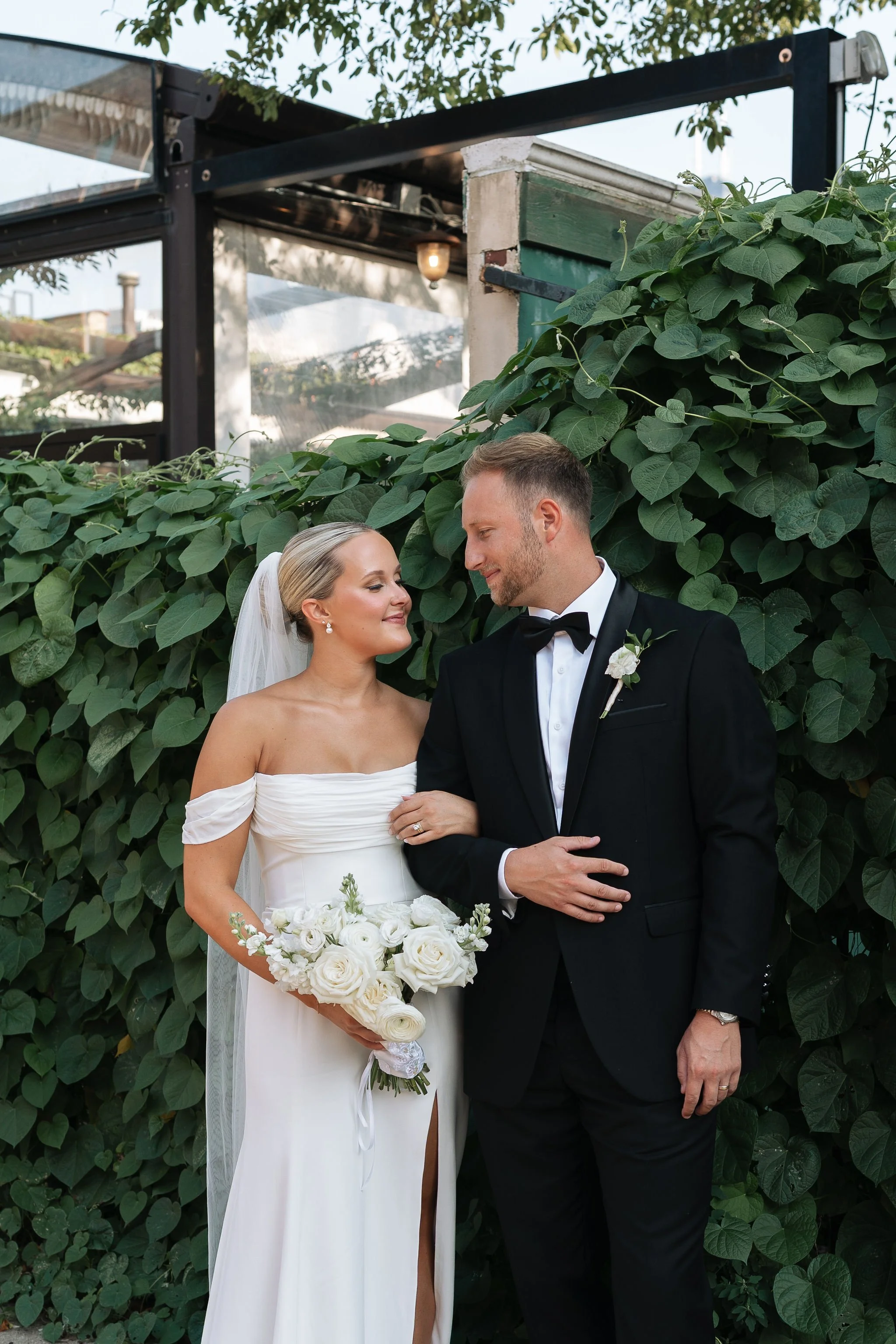 bride and groom looking at each other smiling with green plants as background