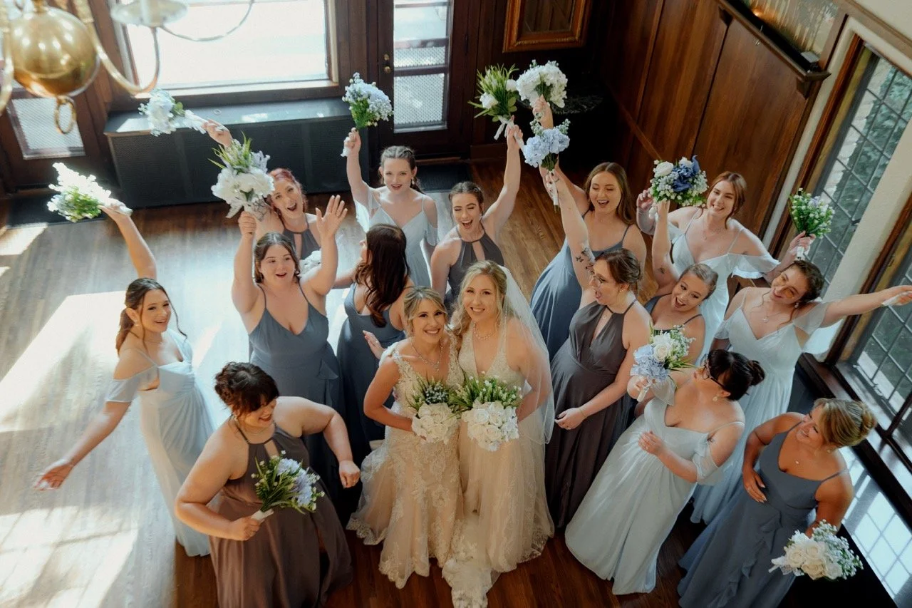 Two brides standing below with wedding party cheering with their hands up
