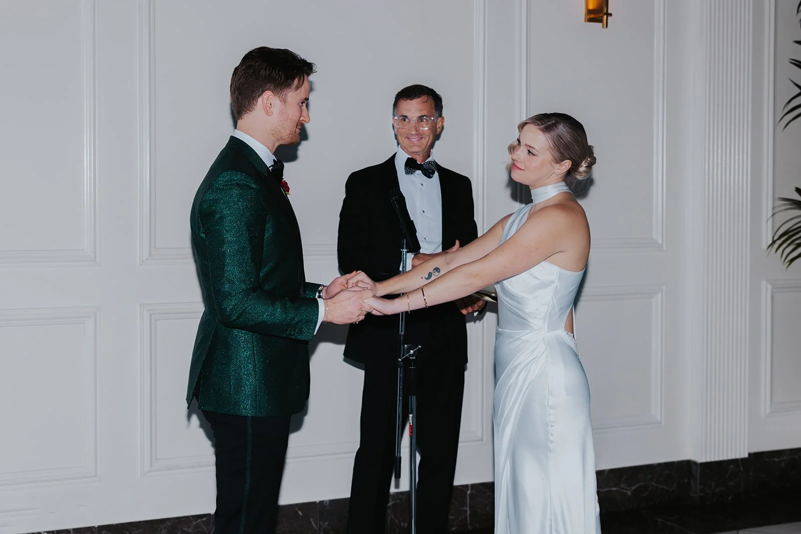 bride and groom grinning and holding hands with officiant smiling at them