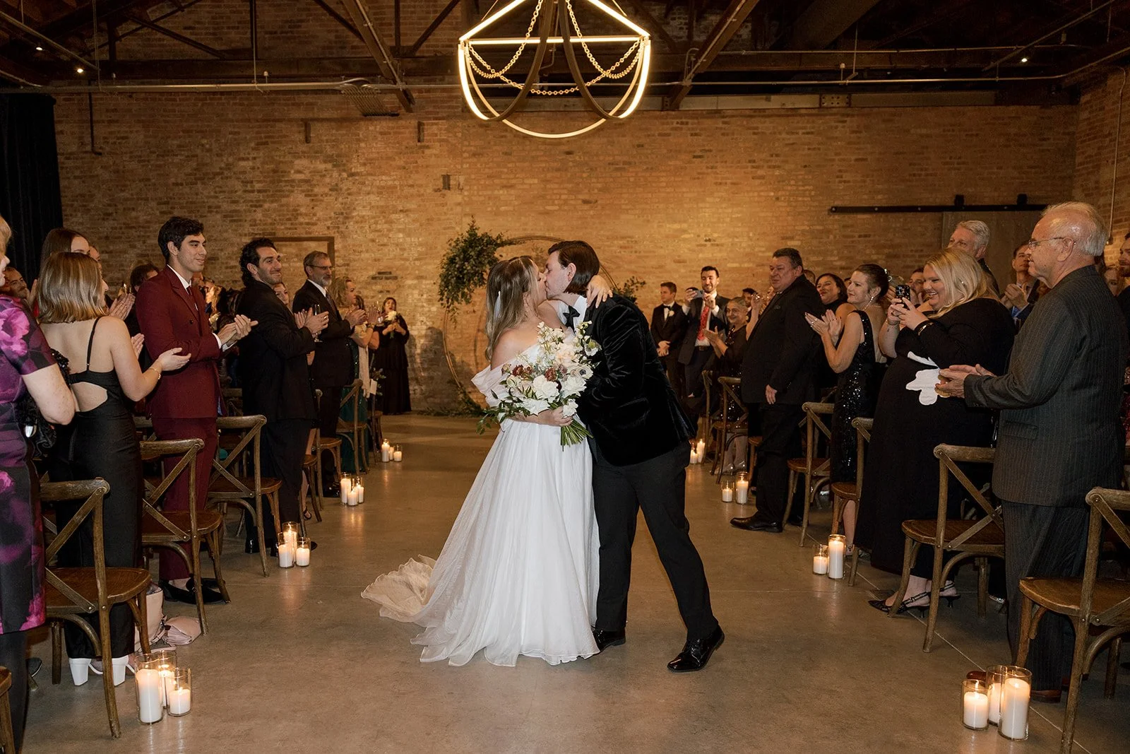 Couple kissing in aisle of wedding ceremony recessional with crowd standing and clapping
