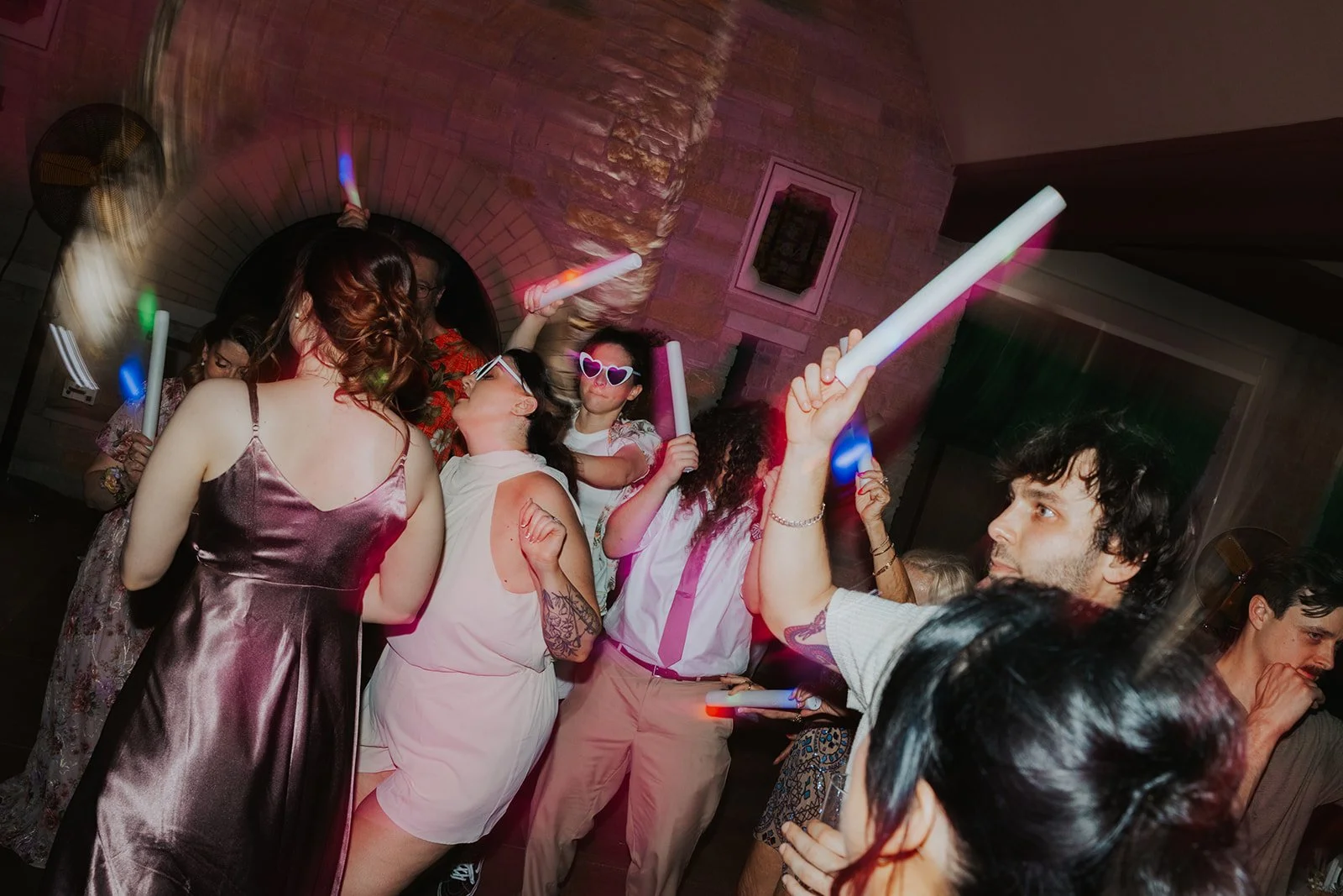Two brides dancing with wedding guests with cool lighting and LED foam glow sticks