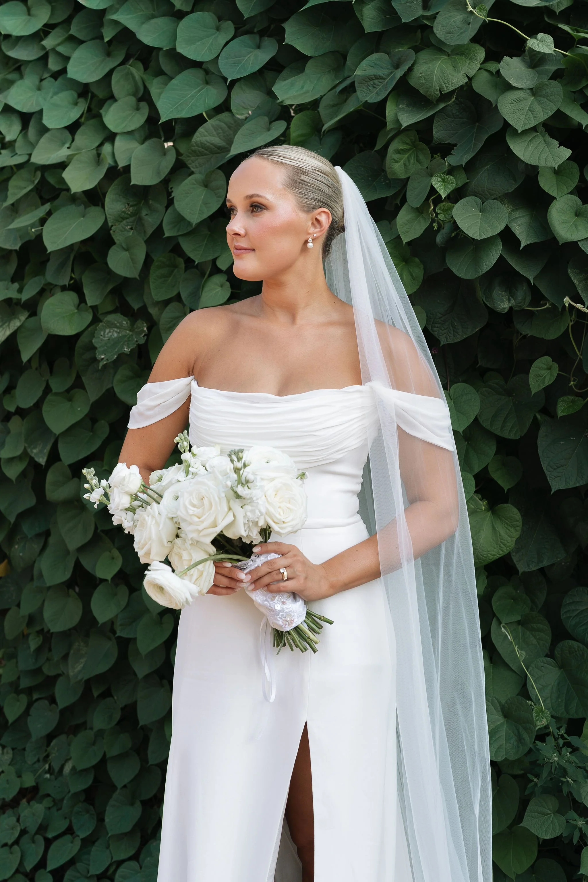 bride looking off and holding bouquet showing off the ruching Greek style of her dress for European style wedding