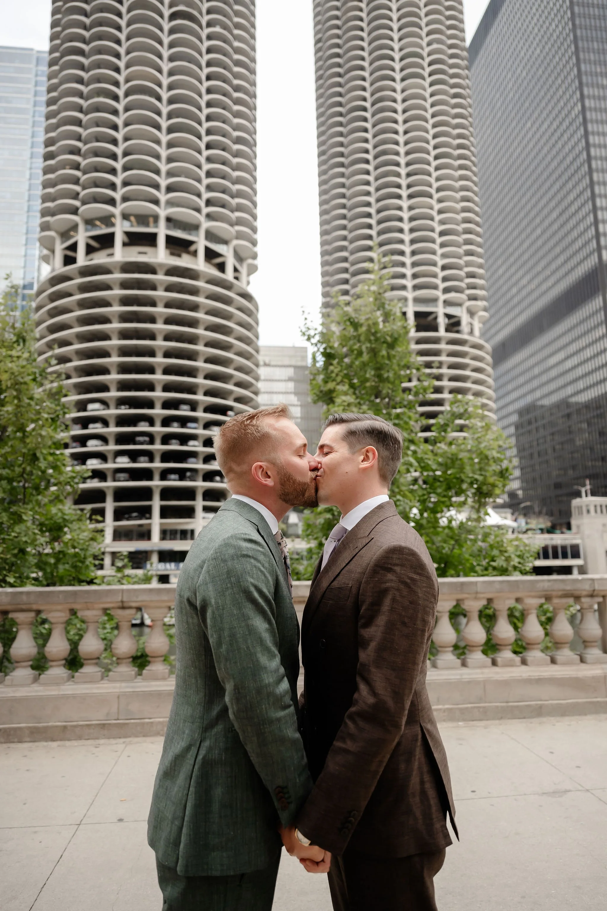 Two grooms kissing with tall buildings as background