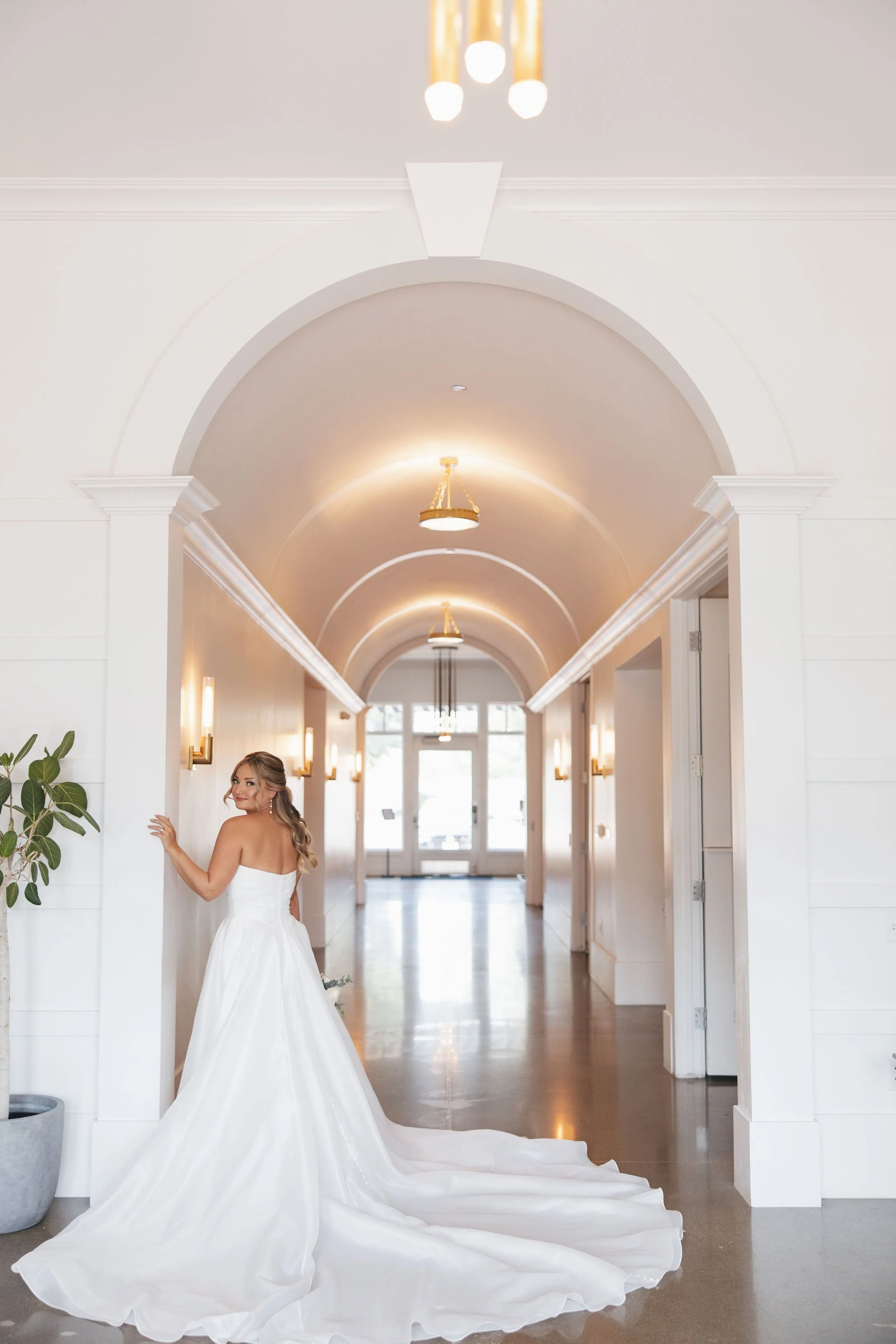 Bride standing against hallway wall showing back of her flowing white wedding dress