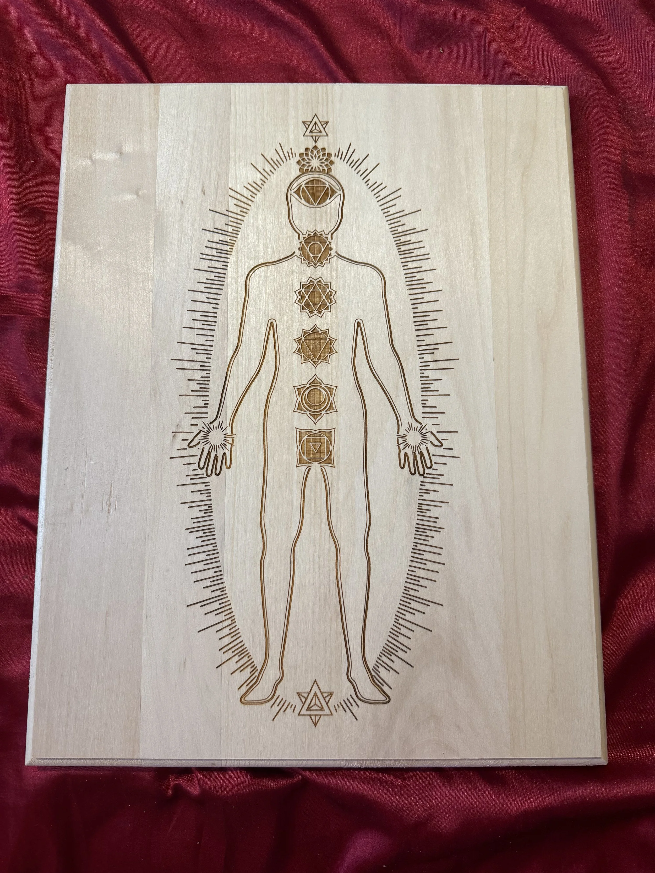 A wood-engraved board centered with a human silhouette showing the seven chakra points, used as a proxy to create a custom crystal grids for distance healing.