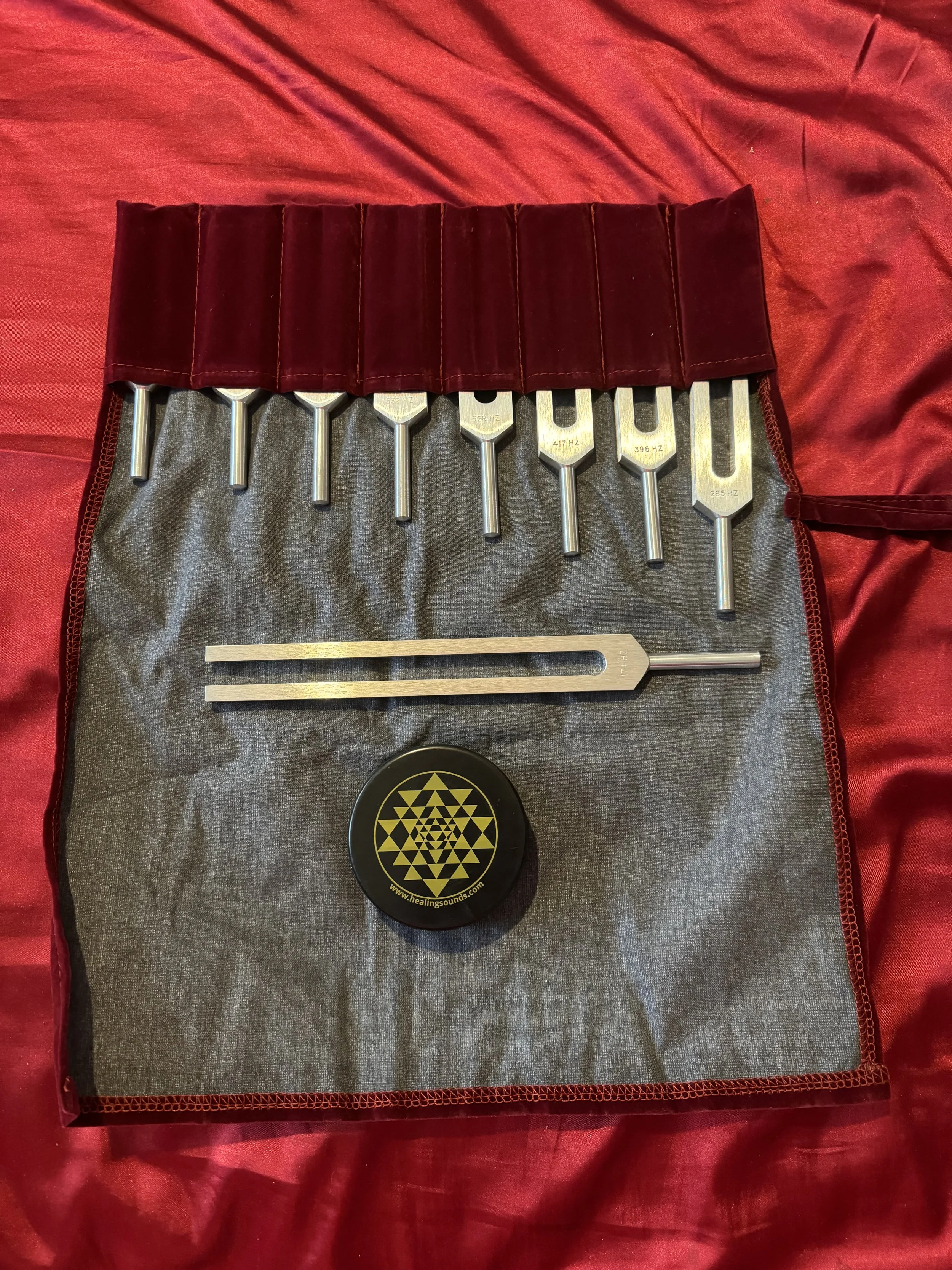 Natasha's professional set of various metal tuning forks in a grey and red carrying case, used for sound healing during Reiki sessions.