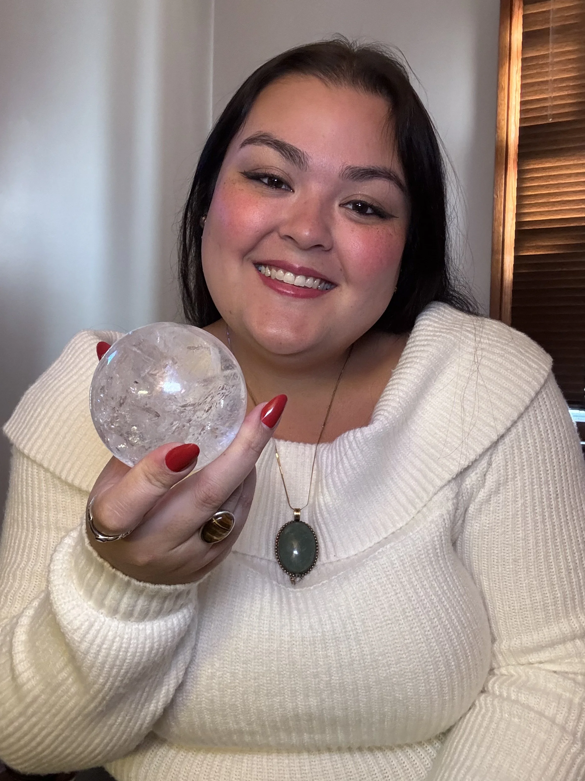 Natasha smiling at the camera holding a clear quartz crystal ball, featured in a circular frame.