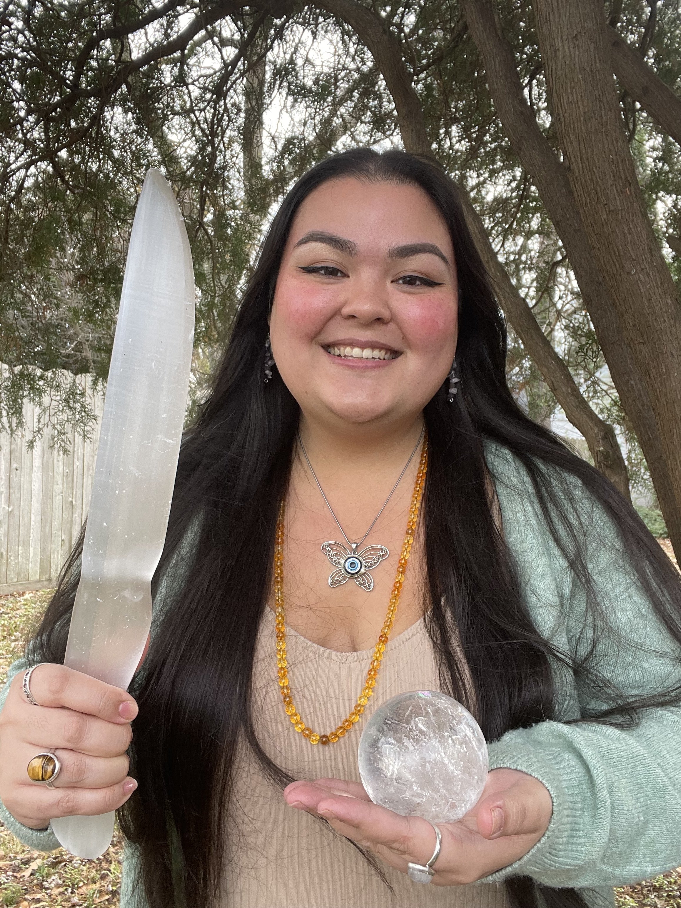 Spiritual Mentor Natasha smiling outdoors, holding a large selenite athame and a clear quartz sphere crystal ball.