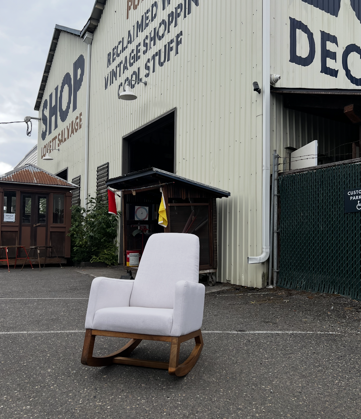 White armchair in parking lot in front of a vintage shop building with signs reading "VINTAGE SHOP" and "TOOLS & STUFF."