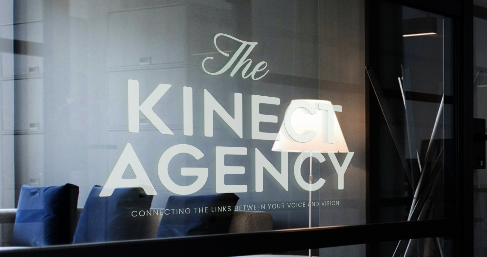 office reception area with glass door displaying the text "The Kinetic Agency" and a subtitle "Connecting the links between your voice and vision"; modern interior with chairs, a floor lamp, and a staircase visible through the glass.