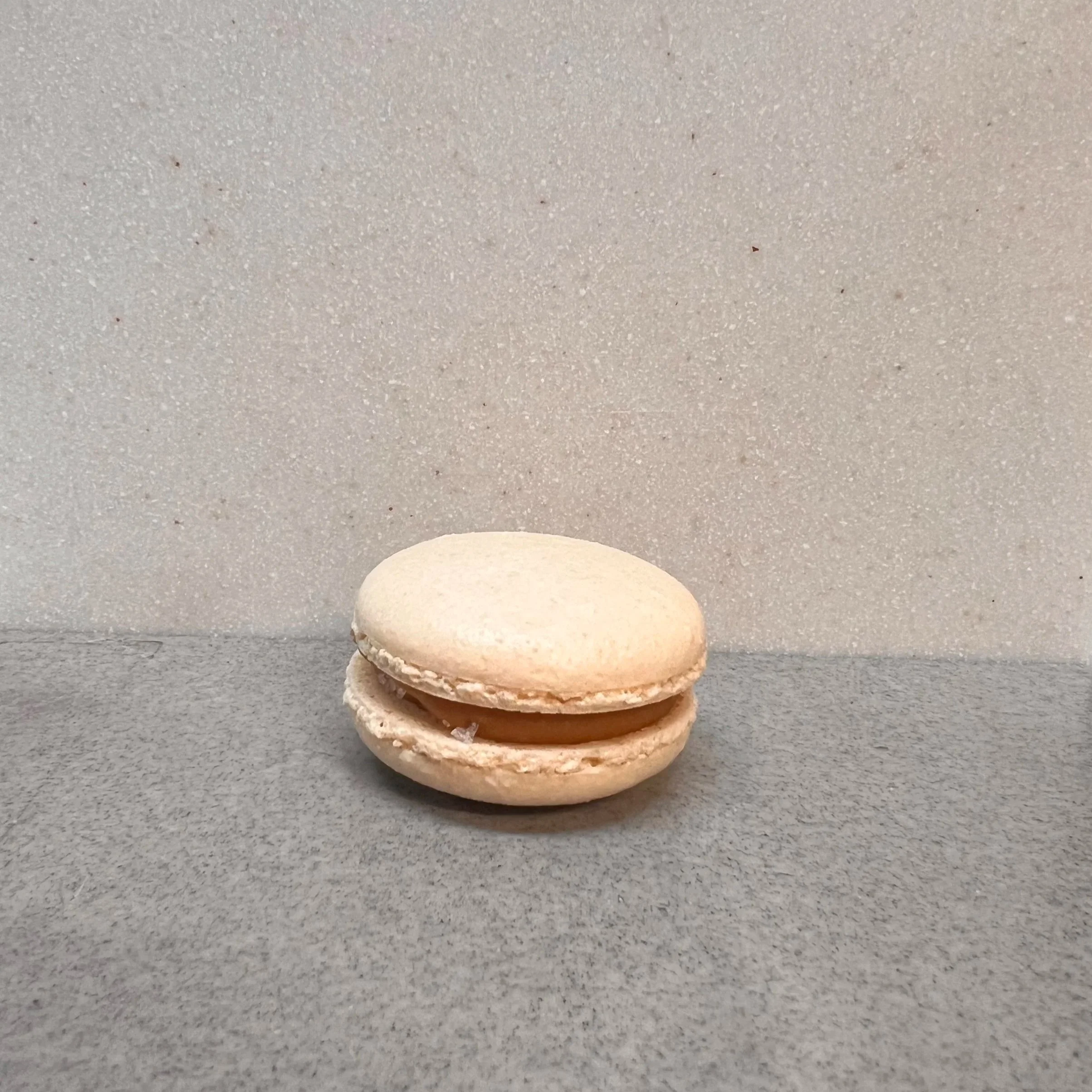 Close-up of a white chocolate macaron with a dark chocolate filling, placed on a dark surface.