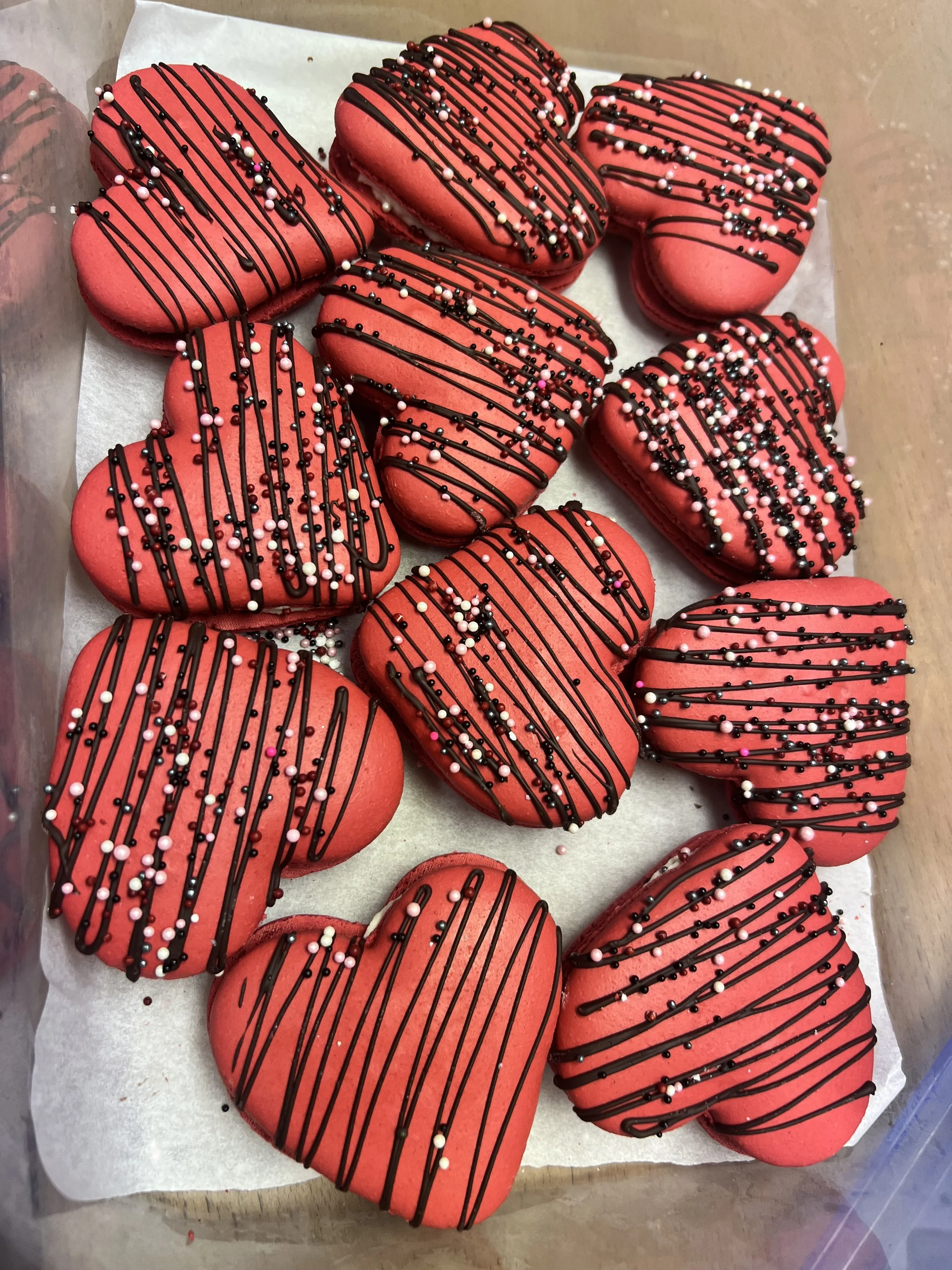 Red heart-shaped cookies decorated with chocolate drizzle and colorful sprinkles.