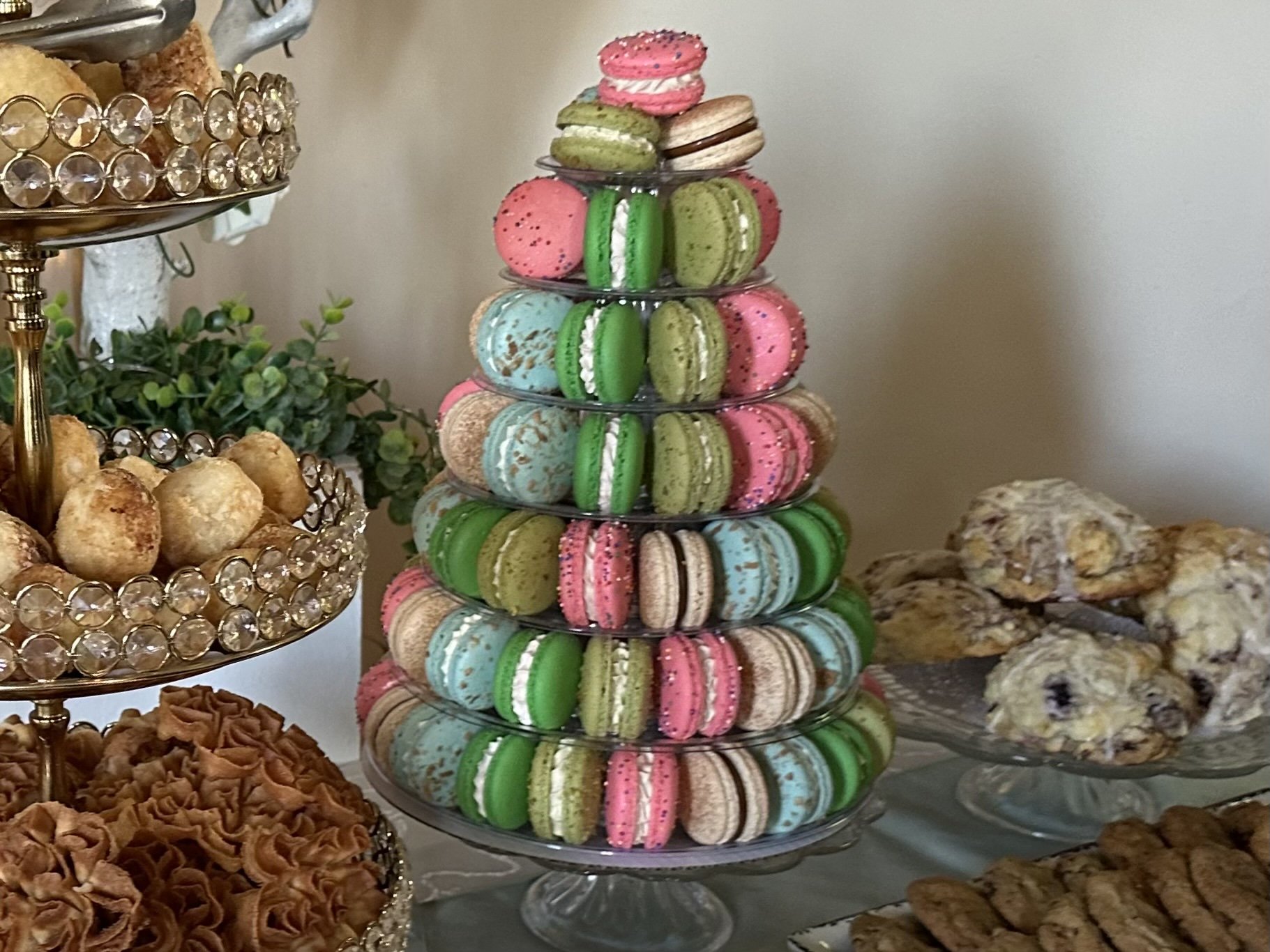 A multi-tiered stand filled with colorful macarons, with other baked goods like cookies and pastries surrounding it.