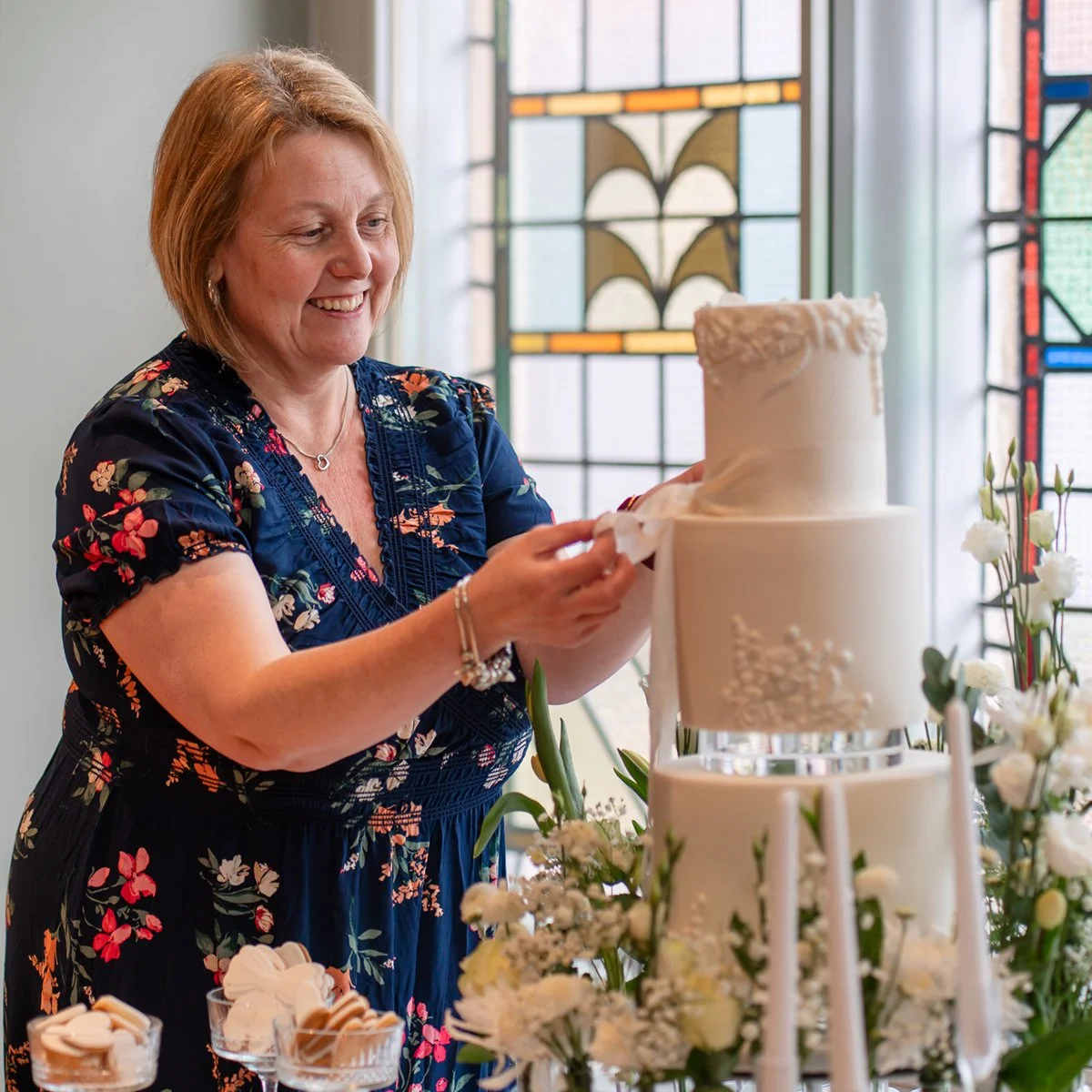 Sarh from Cakes by Mrs F setting up a white tiered wedding cake in front of a stained glass window