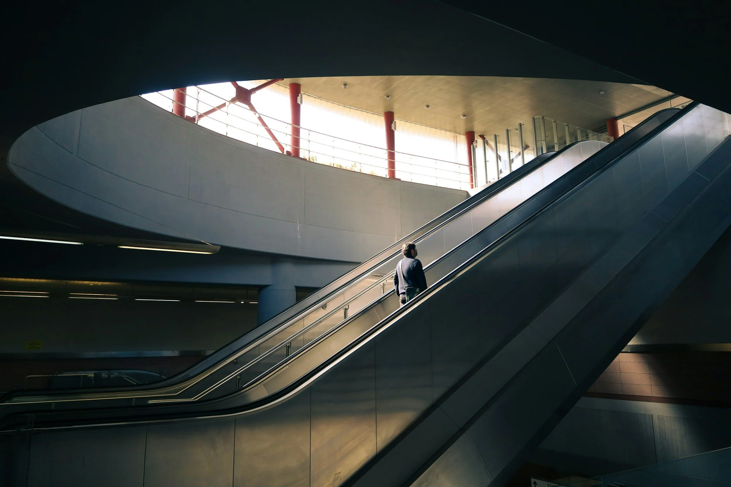 Person on an escalator in a modern building with natural light streaming in through windows.
