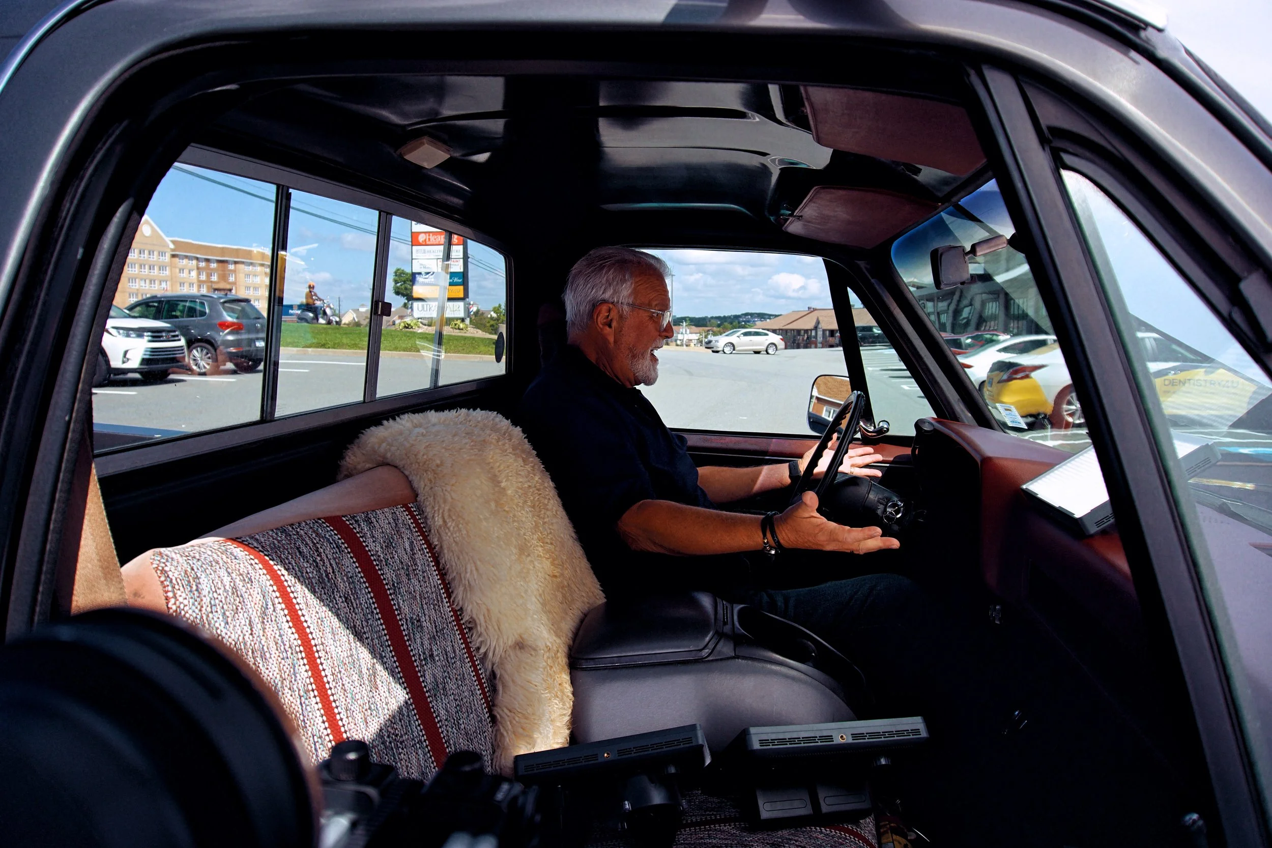 Man sitting inside a parked car in a parking lot, holding a steering wheel.