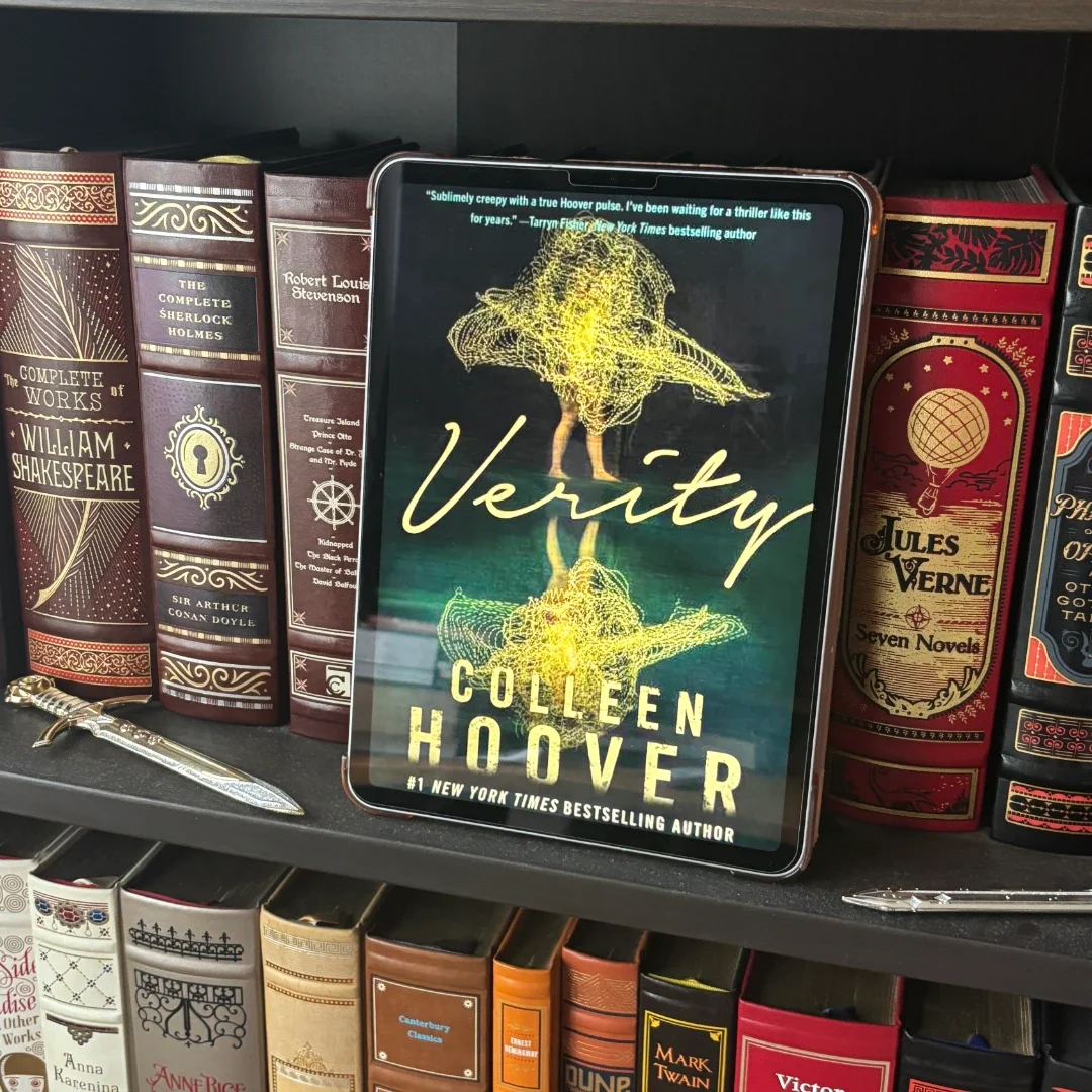 Verity by Colleen Hoover displayed on a tablet sitting on a book shelf surrounded by beautiful books