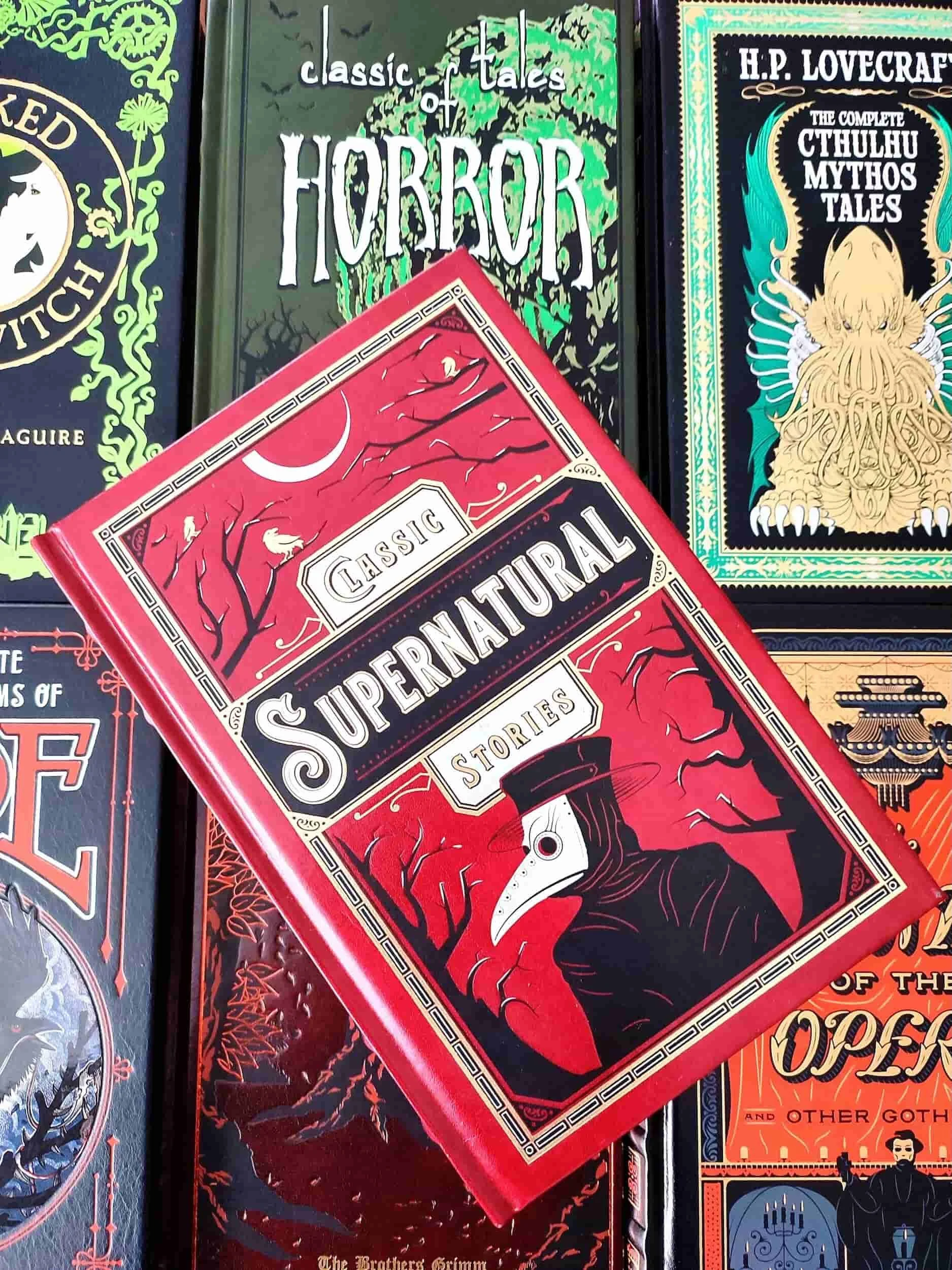 Red leatherbound edition of Classic Supernatural Stories, featuring a plague doctor mask on the front, sitting on top of 6 other classic horror books 2026